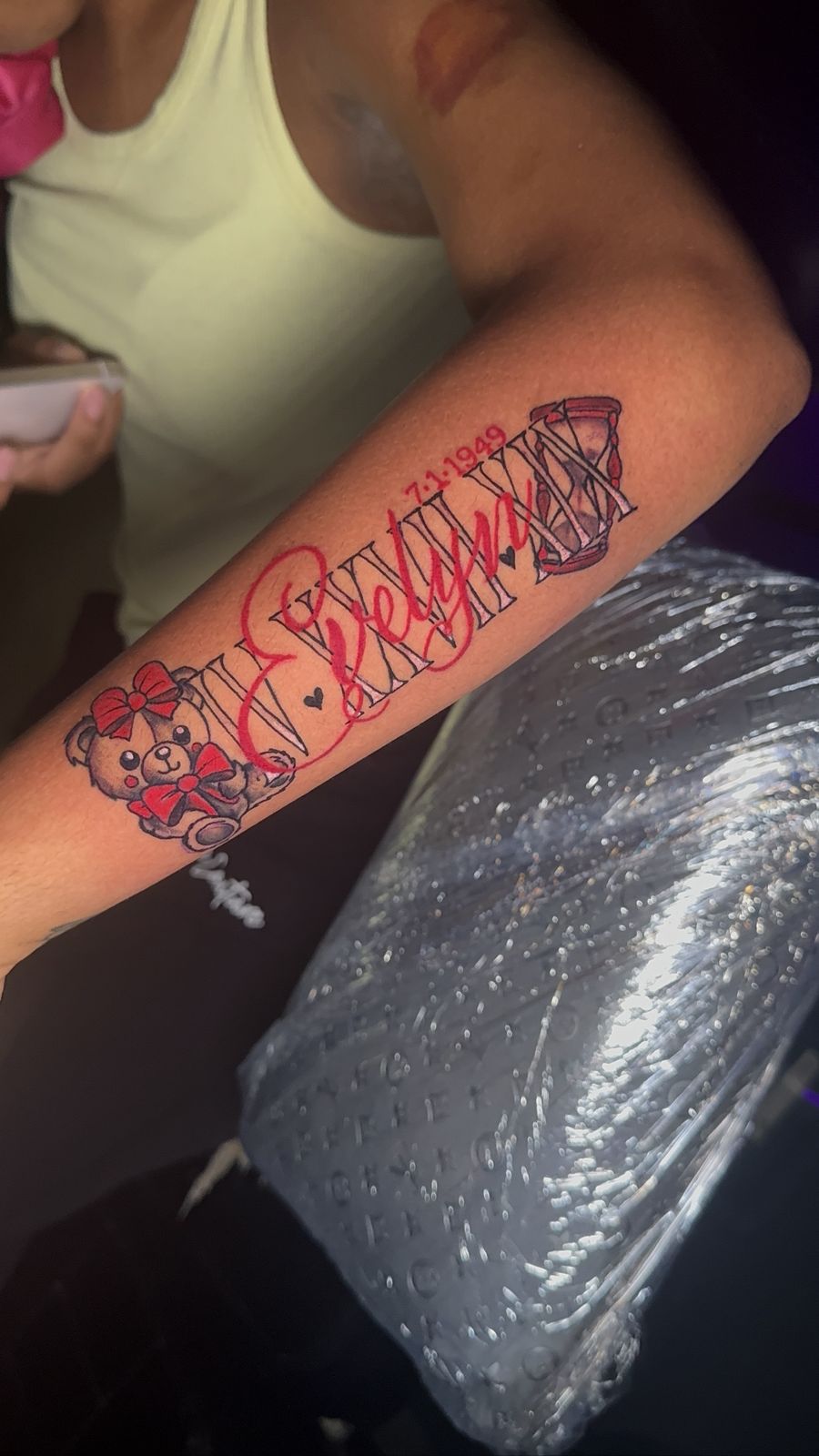 Script name tattoo with teddy bear and hourglass, red ink